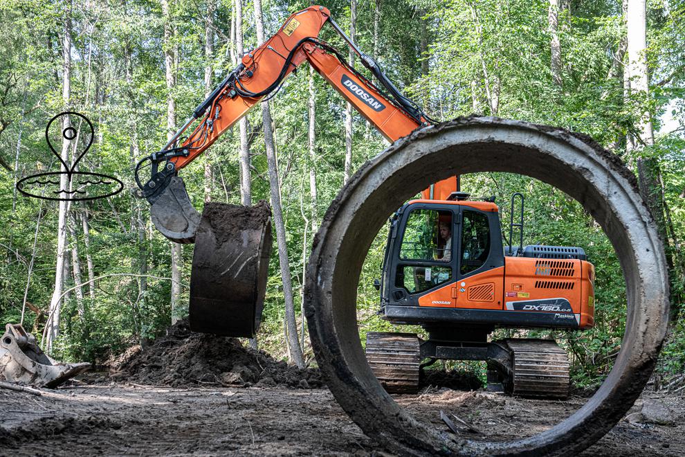 Grävskopa i bakgrund. Stor ring av betong i förgrund.