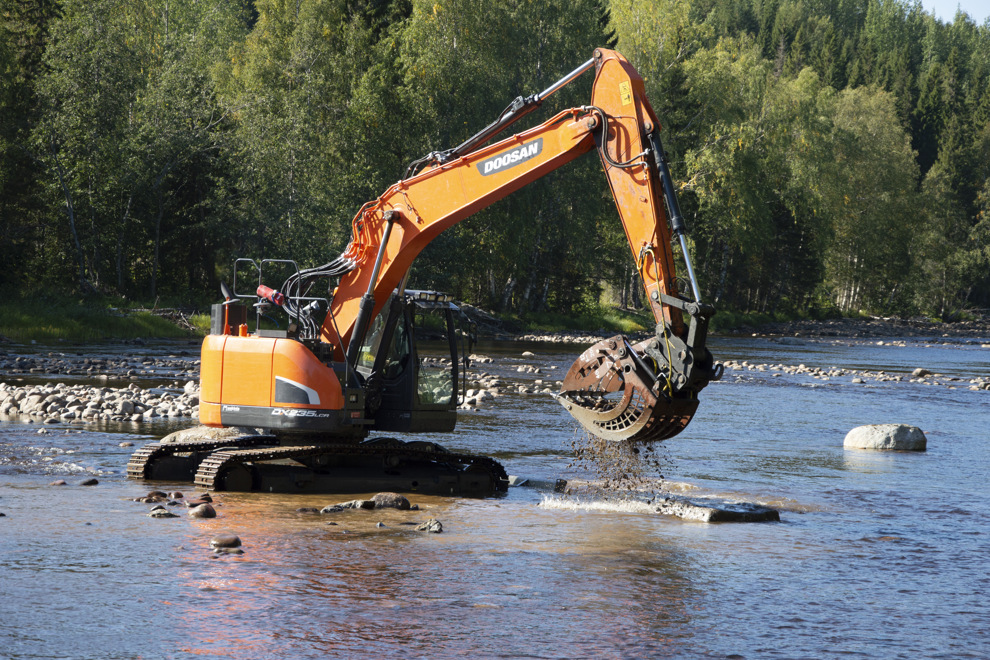 En orange grävmaskin står mitt i en flod.