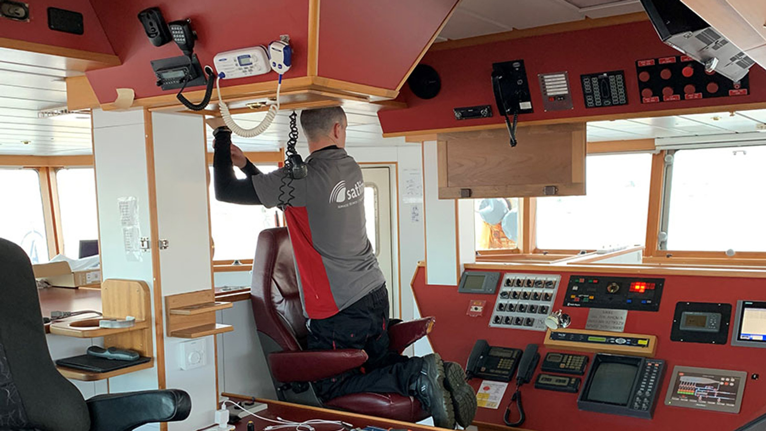 En man står på knä på en stol och installerar kamerautrustning i styrhytten på en fiskebåt