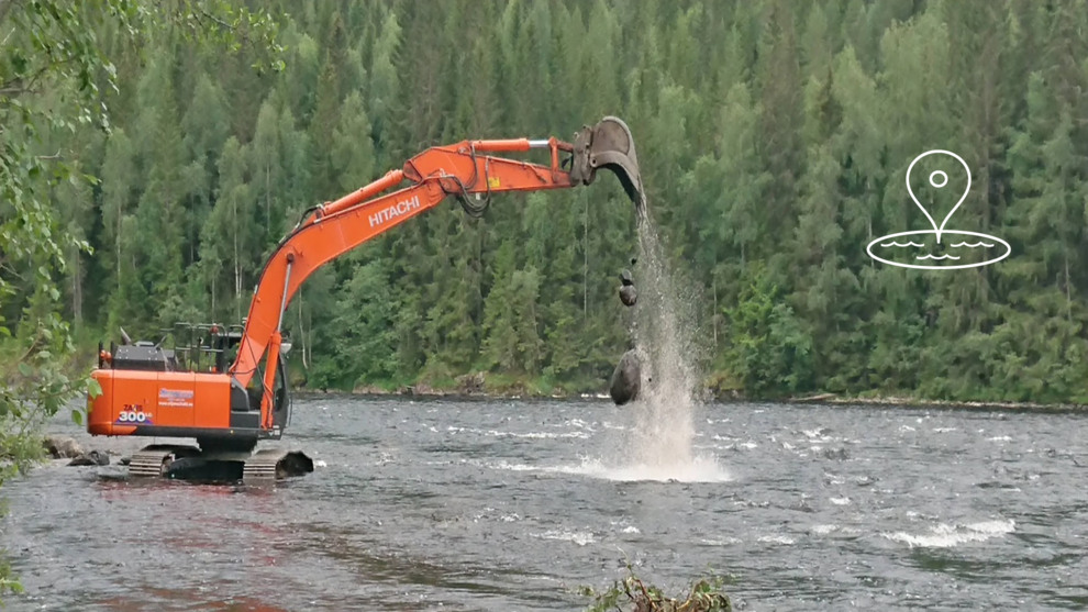 Grävare i vattendrag. Flyttar på större stenar.