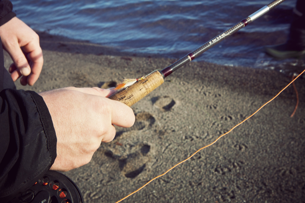 En man som står bredvid en vattendrag och håller i ett fiskespö.
