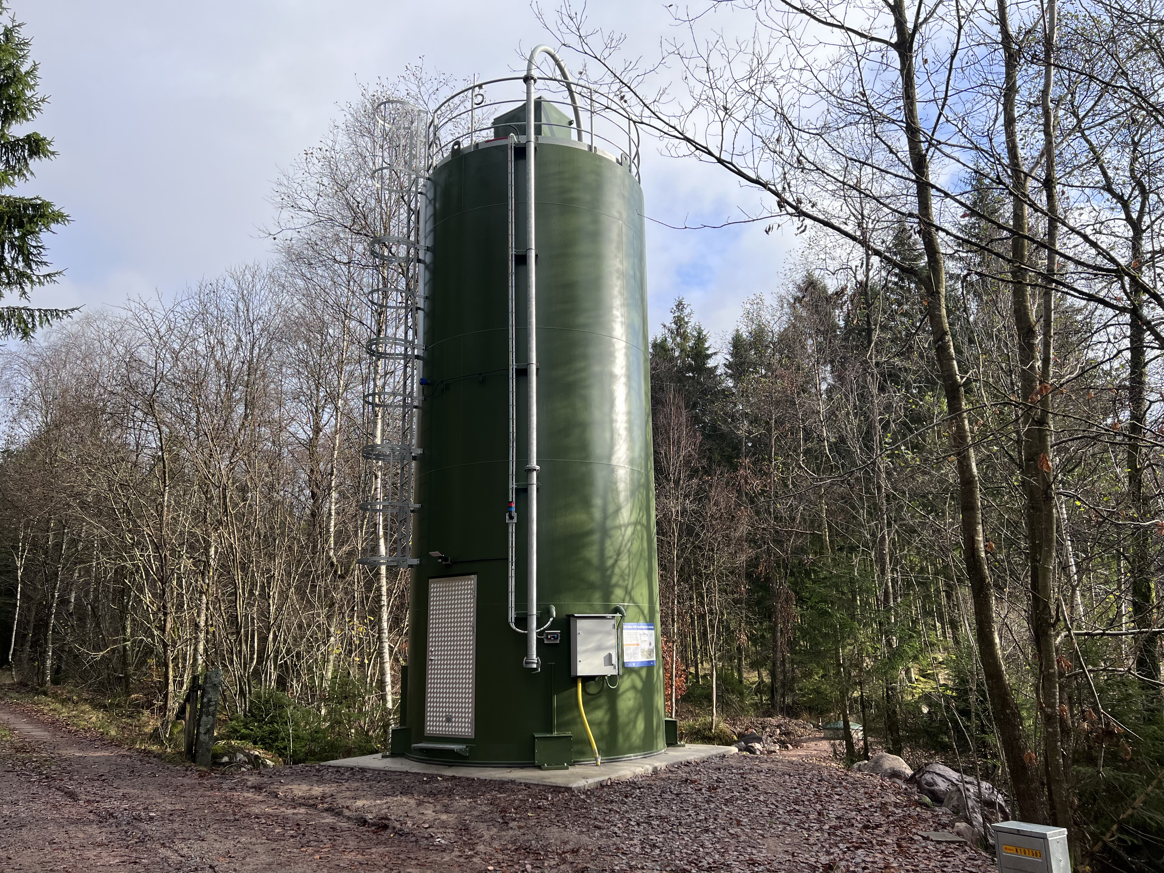 kalkdoserare - en stor grön cylinderformad behållare som står på betongplatta i skog vid vatten.