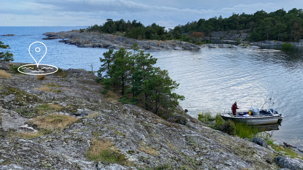 Skärgårdsmiljö. Vid klippkanten ligger en båt. En man står i båten.