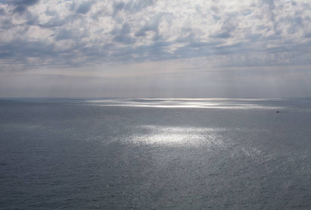 Molnen spricker upp och solstrålar kommer fram, lyser ned på havet. 