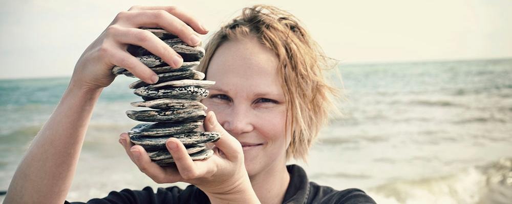 Kvinna håller uppe stenar. Havet i bakgrunden