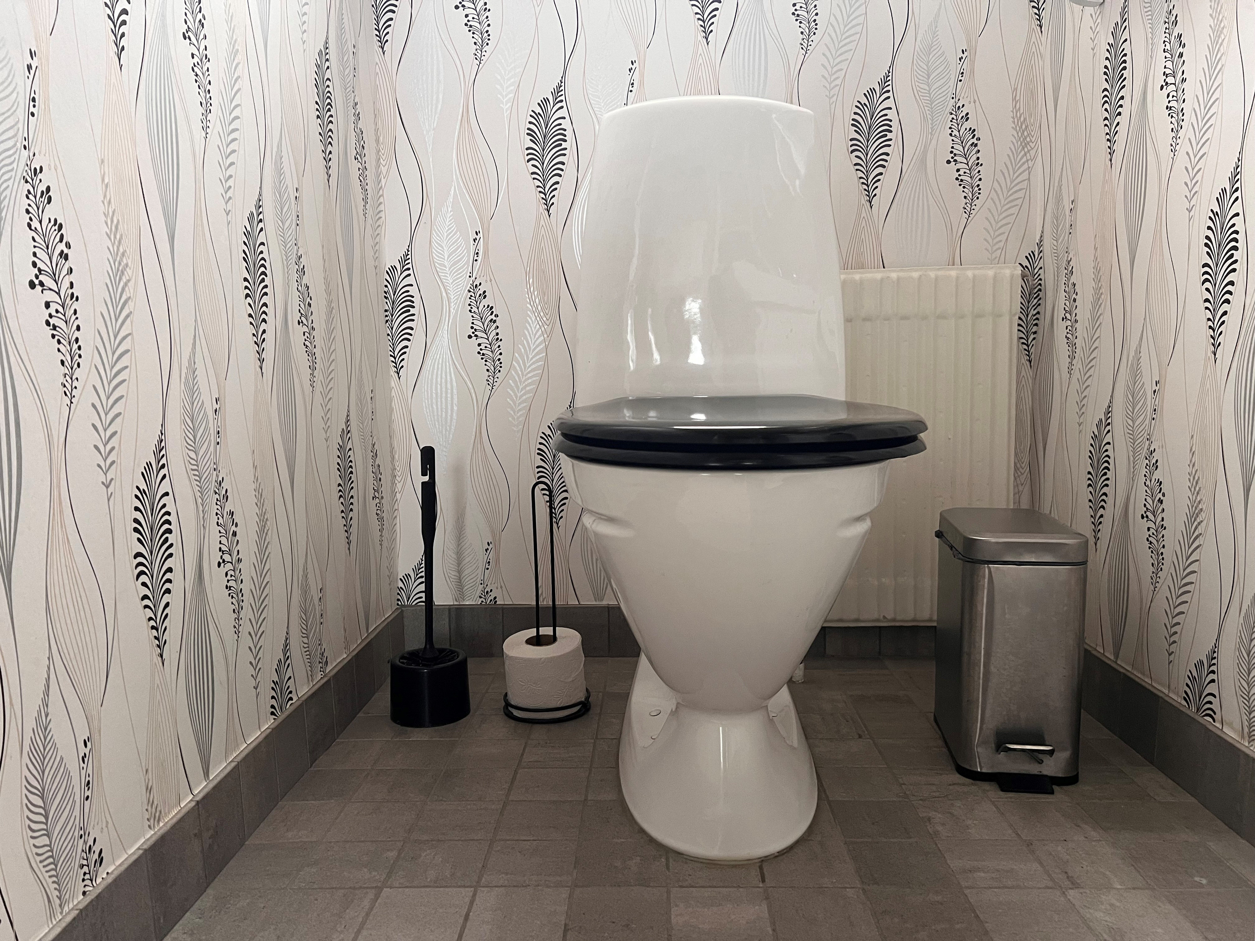 Toalettstol med papperskorg, toaborste och extra toapappersrulle.