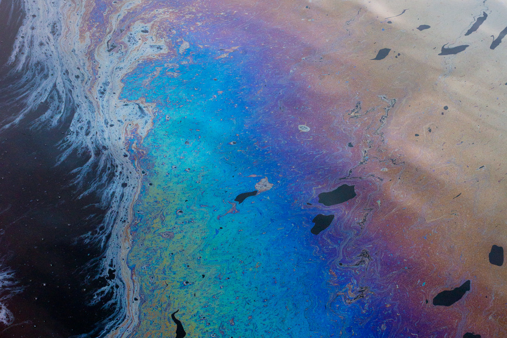 Olja flyter på vattenytan och skimrar i blått och lila.