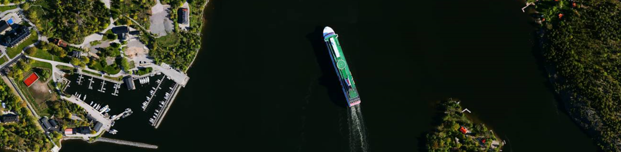 Flygfoto på kustlinje med hamn. Fartyg på väg in i hamnen.